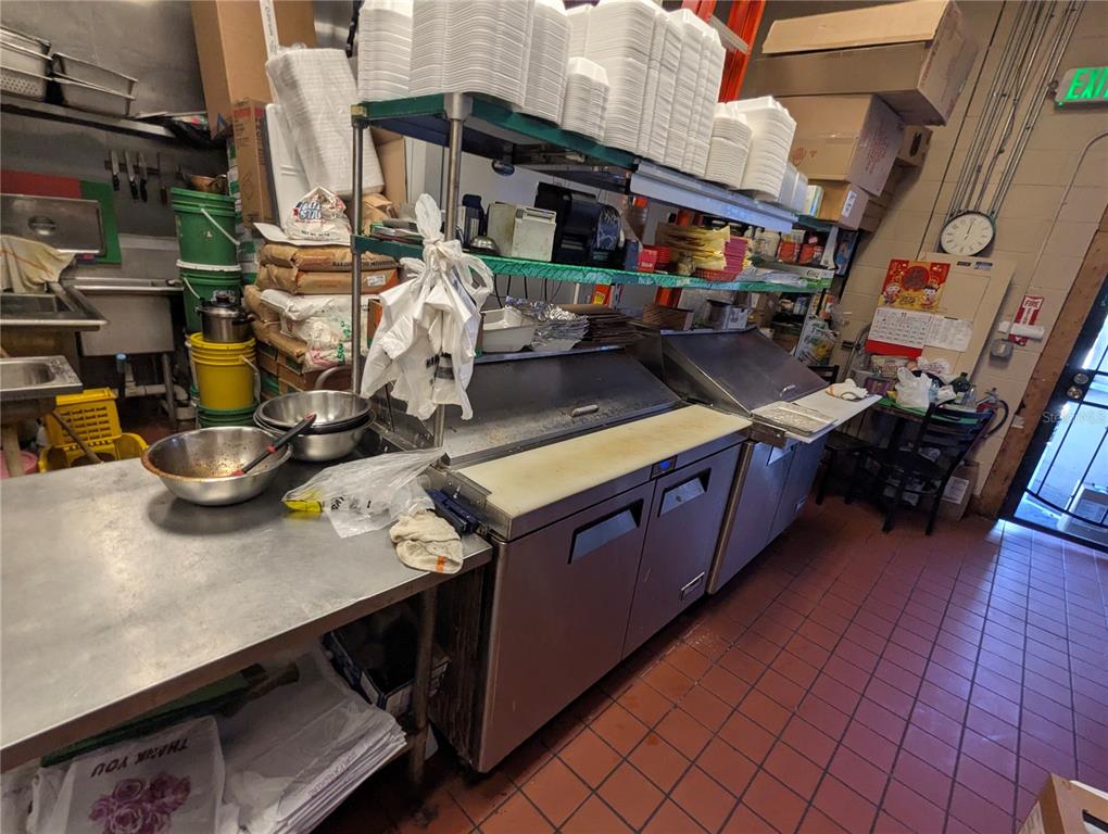 A commercial kitchen features stainless steel prep tables, a refrigeration unit, and stacked takeout containers — 2430 US HIGHWAY 27 UNIT 380, CLERMONT, FL