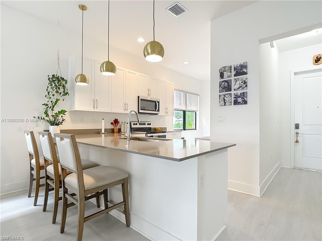 A modern kitchen features white cabinetry, a quartz island with bar seating, and pendant lighting — 5696 Argento Dr, Ave Maria FL 34142, AVE MARIA, FL