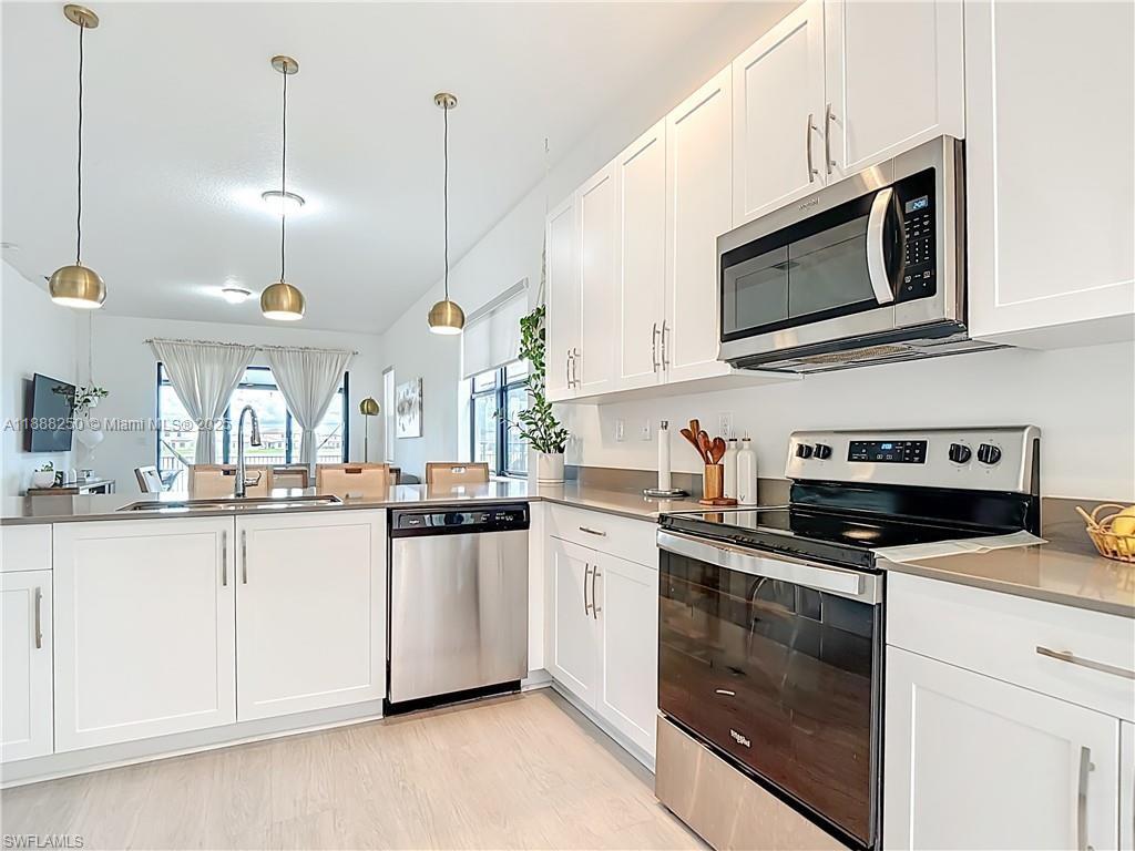 A modern kitchen features white cabinets, stainless steel appliances, and a breakfast bar island — 5696 Argento Dr, Ave Maria FL 34142, AVE MARIA, FL