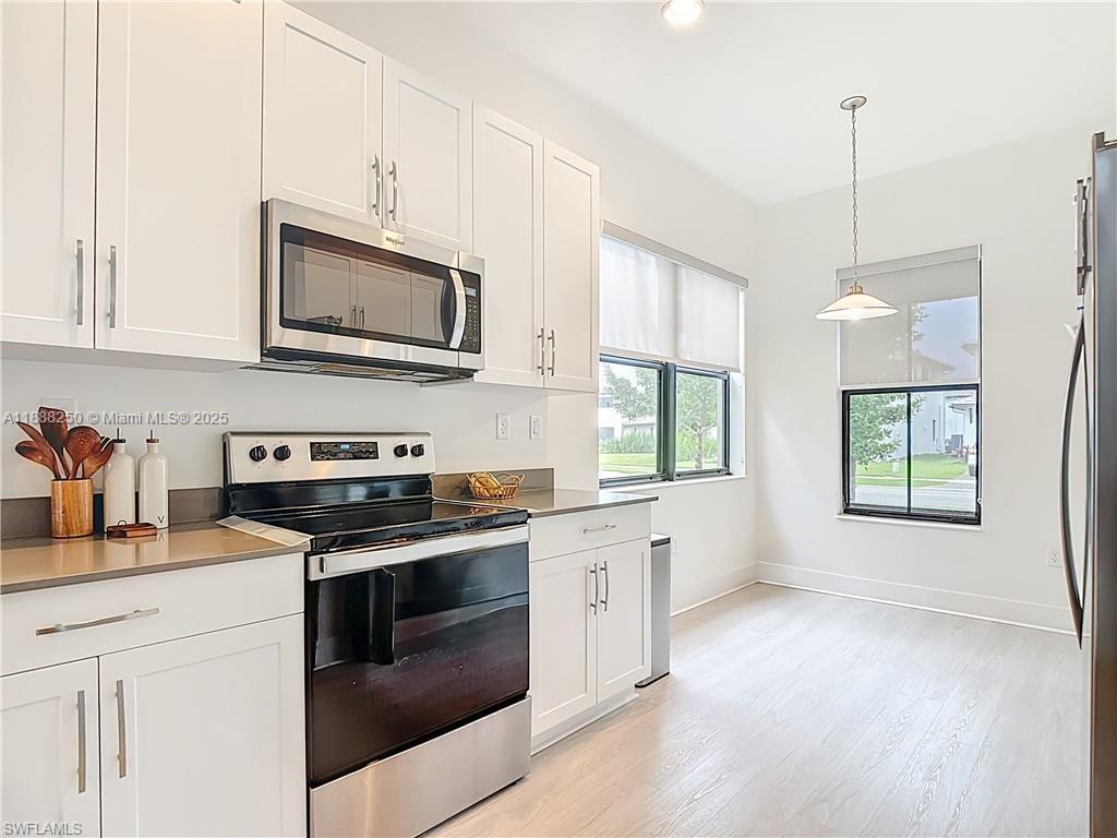 A modern kitchen features white cabinets, stainless steel appliances, and light-colored wood flooring — 5696 Argento Dr, Ave Maria FL 34142, AVE MARIA, FL