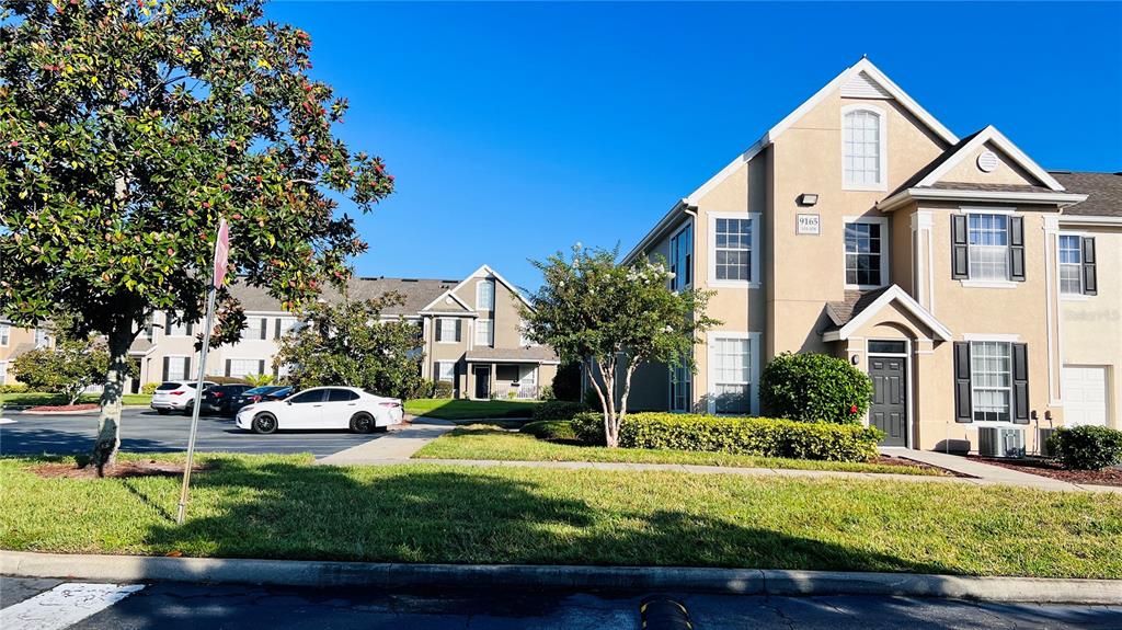 A multi-story tan apartment building with a parking lot and trees in the foreground — 9165 LEE VISTA BOULEVARD UNIT 108, ORLANDO, FL