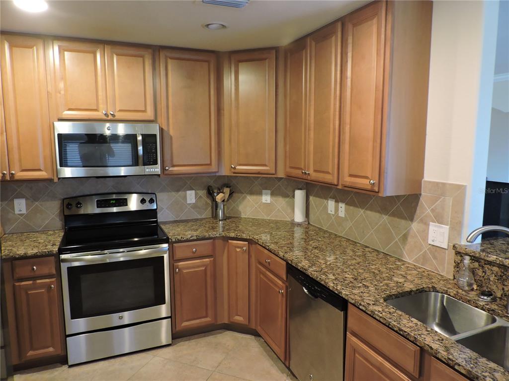 A kitchen featuring wood cabinets, granite countertops, stainless steel appliances, and a tiled backsplash — 20201 RAGAZZA CIRCLE UNIT 102, VENICE, FL