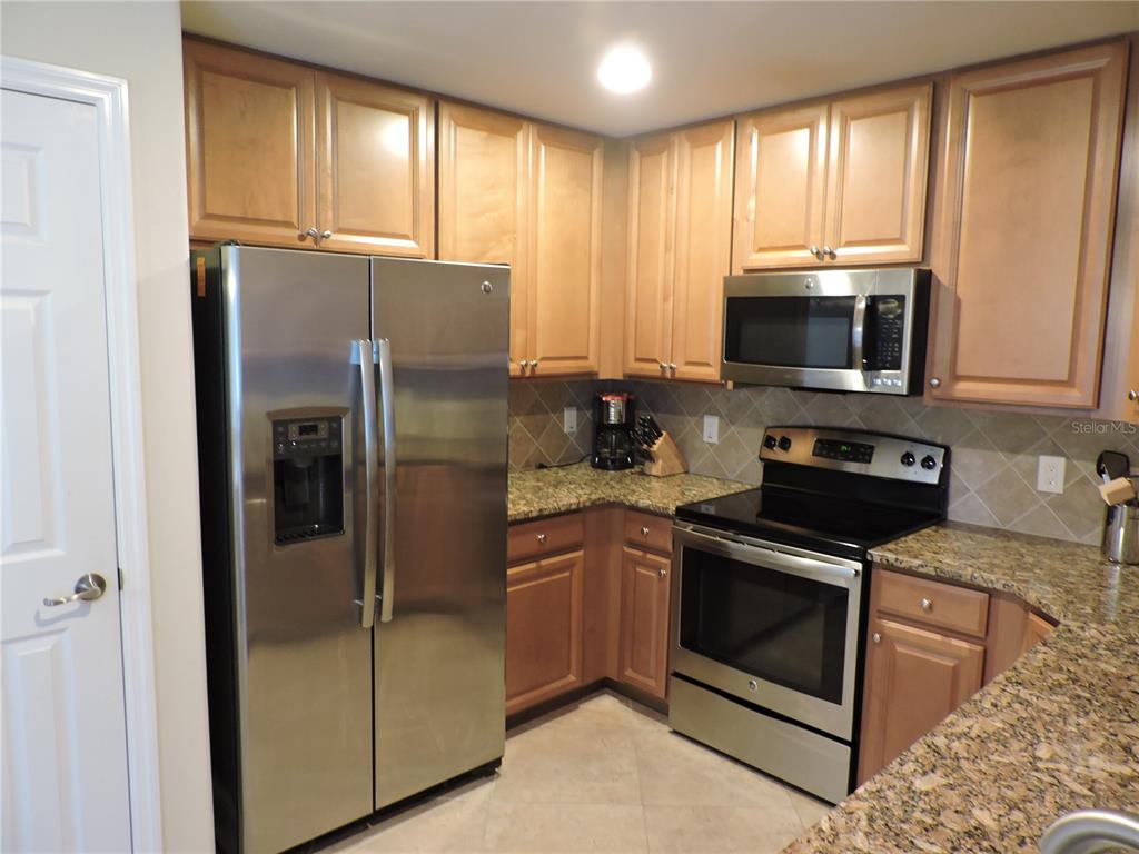 A kitchen features stainless steel appliances, light wood cabinets, and granite countertops — 20201 RAGAZZA CIRCLE UNIT 102, VENICE, FL