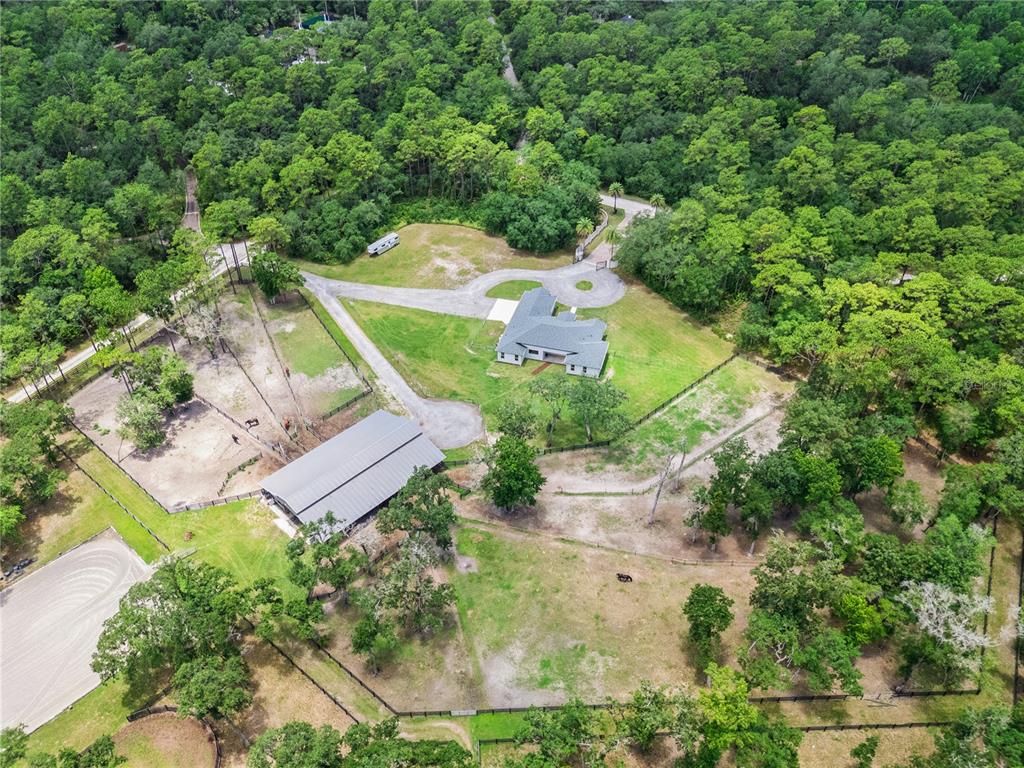 An aerial view shows a house, a large barn, and fenced pastures surrounded by trees — 2370 PINE MEADOWS PLACE, OVIEDO, FL