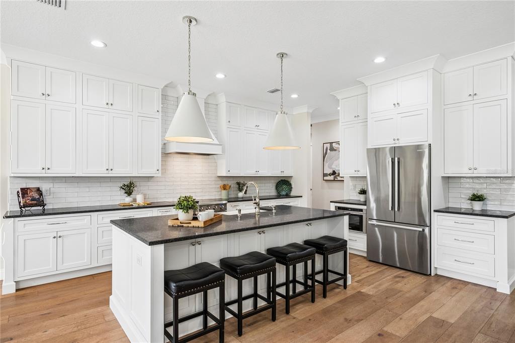A modern kitchen features white cabinetry, a dark stone island with seating, and hardwood floors — 2370 PINE MEADOWS PLACE, OVIEDO, FL