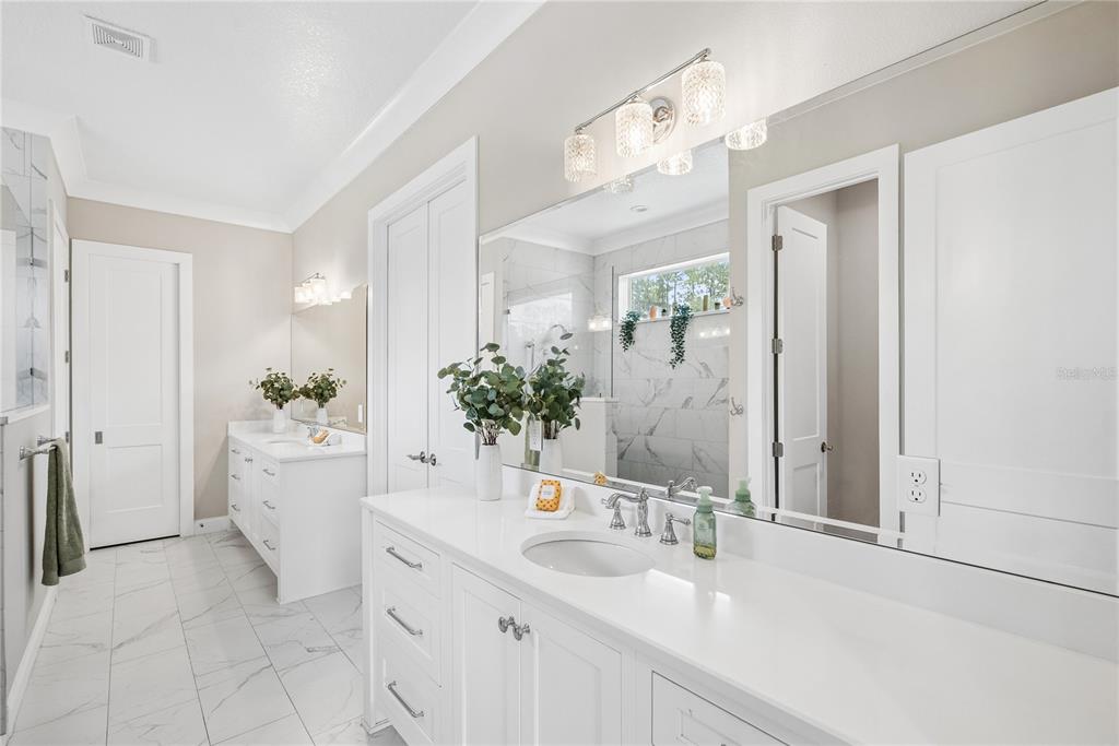 A bright bathroom features white double vanities, marble-look tile flooring, and a large wall mirror — 2370 PINE MEADOWS PLACE, OVIEDO, FL