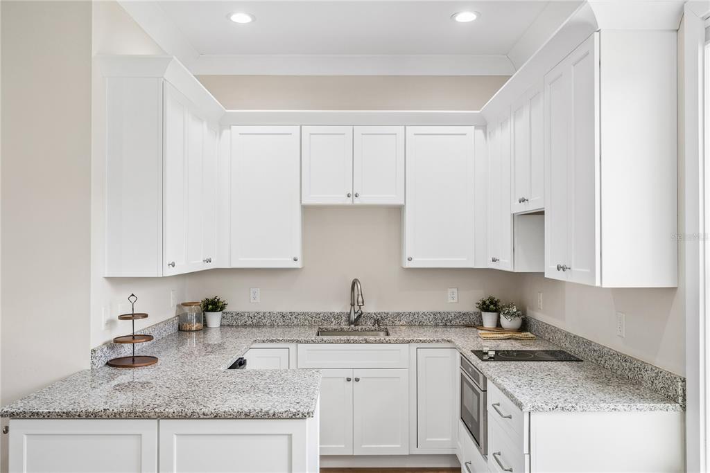 A kitchen features white cabinets, granite countertops, a stainless steel sink, and a built-in cooktop — 2370 PINE MEADOWS PLACE, OVIEDO, FL