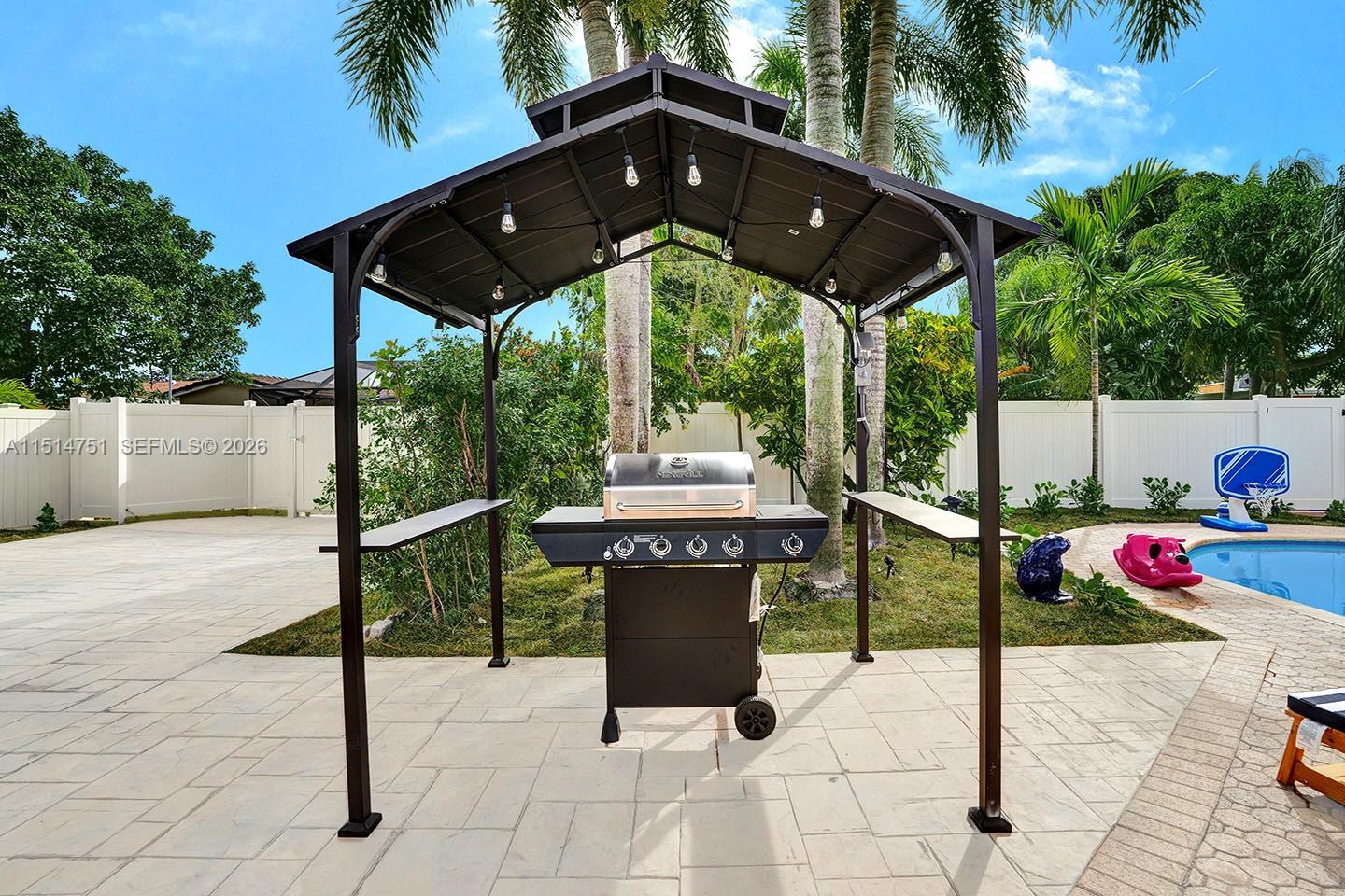 A black metal grill gazebo stands on a paved patio next to a swimming pool — 5500 Cleveland St, Hollywood FL 33021, HOLLYWOOD, FL