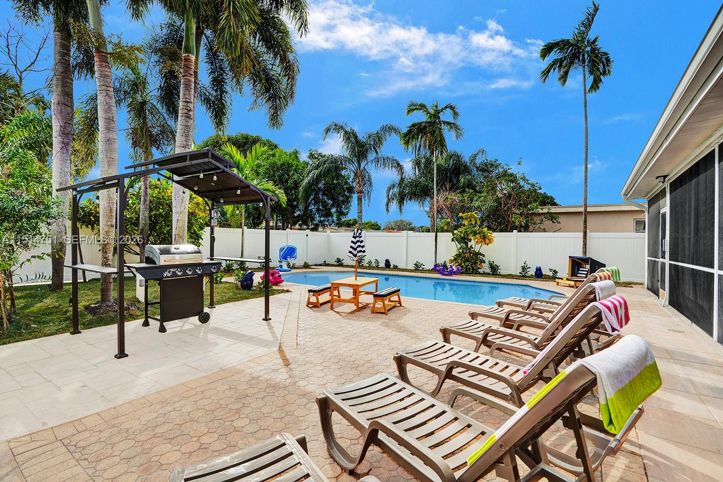 A backyard patio features a swimming pool, lounge chairs, a grill station, and palm trees — 5500 Cleveland St, Hollywood FL 33021, HOLLYWOOD, FL