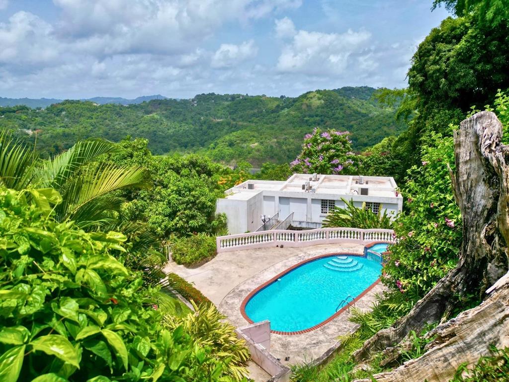An outdoor swimming pool sits in front of a white building surrounded by lush hills — D 17 SUNSET HILLS, GUAYNABO, PR