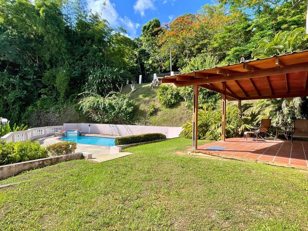 A swimming pool and a covered patio with a tiled floor sit in a grassy yard — D 17 SUNSET HILLS, GUAYNABO, PR