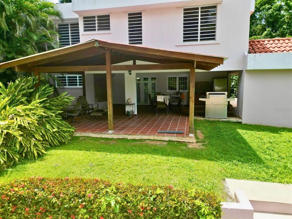 A covered patio with tiled flooring sits adjacent to a two-story house and lawn — D 17 SUNSET HILLS, GUAYNABO, PR