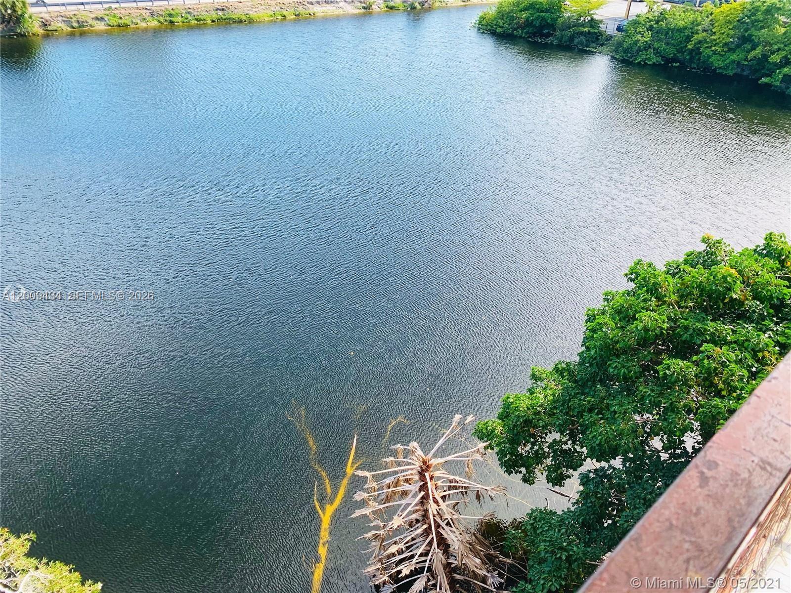 An elevated view looks down over a calm lake bordered by trees and vegetation — 1325 W 68th St # 514, Hialeah FL 33014, HIALEAH, FL
