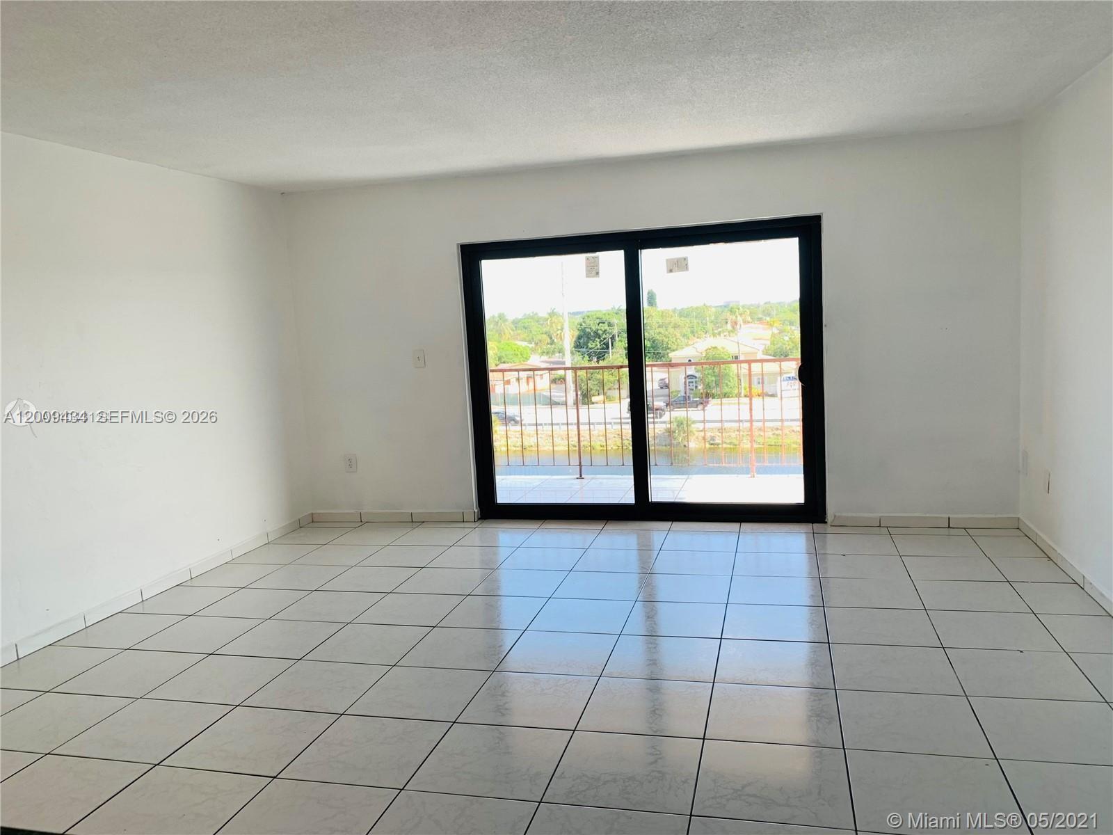 A bright, empty room features white walls, white tile flooring, and a sliding glass door — 1325 W 68th St # 514, Hialeah FL 33014, HIALEAH, FL
