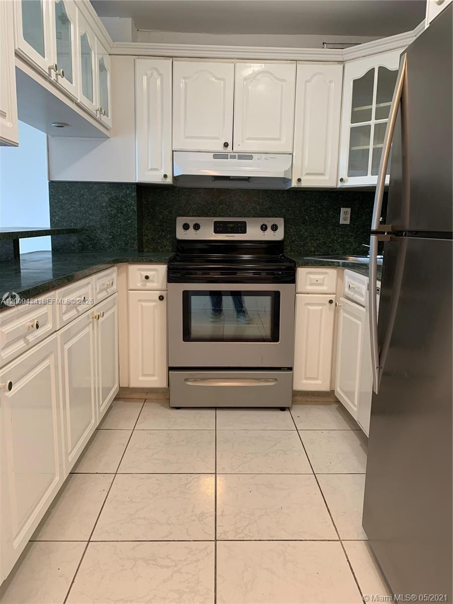 A kitchen features white cabinets, stainless steel appliances, dark countertops, and light-colored tiled flooring — 1325 W 68th St # 514, Hialeah FL 33014, HIALEAH, FL