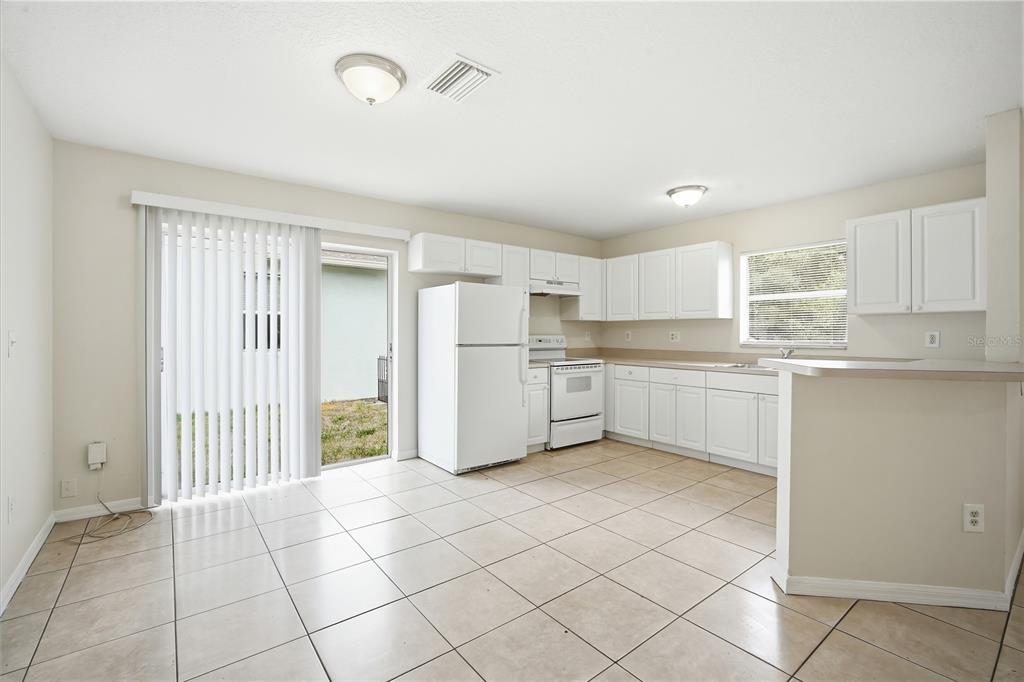 A kitchen with white cabinets, white appliances, and light-colored tile flooring leads to a patio — 3716 N 31ST STREET, TAMPA, FL