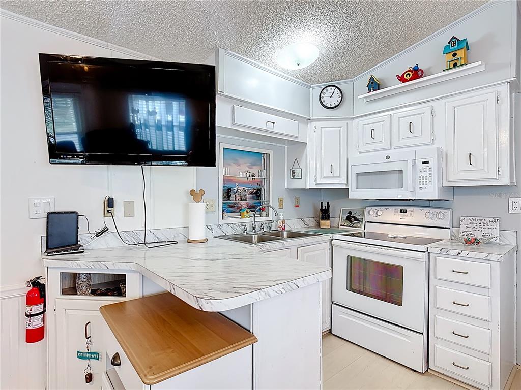 A kitchen features white cabinets, marble-look countertops, a mounted television, and a white stove — 9000 US HWY 192 UNIT 763, CLERMONT, FL