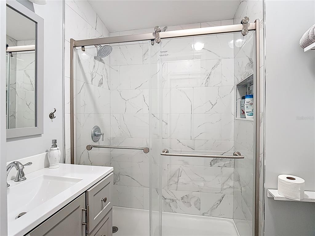 A bathroom features a gray vanity, a white sink, and a glass-enclosed marble-tiled shower — 9000 US HWY 192 UNIT 763, CLERMONT, FL