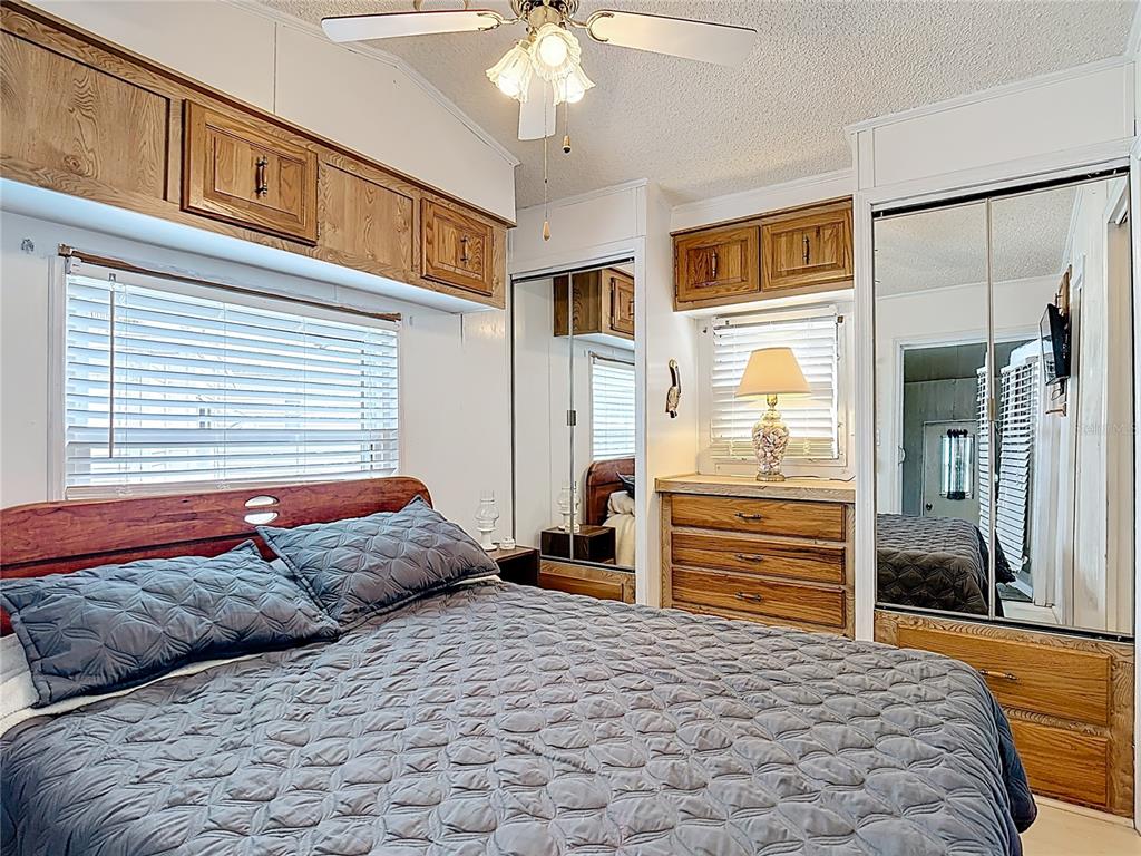 A bedroom features a bed, wooden cabinetry, mirrored closet doors, and a ceiling fan — 9000 US HWY 192 UNIT 763, CLERMONT, FL