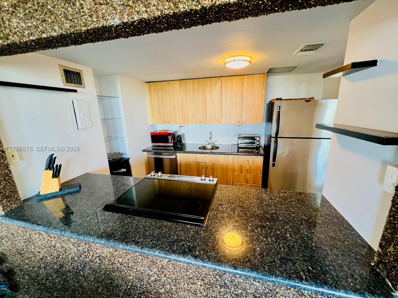 A kitchen features light wood cabinets, dark granite countertops, and stainless steel appliances — 900 Bay Dr # 411, Miami Beach FL 33141, MIAMI BEACH, FL
