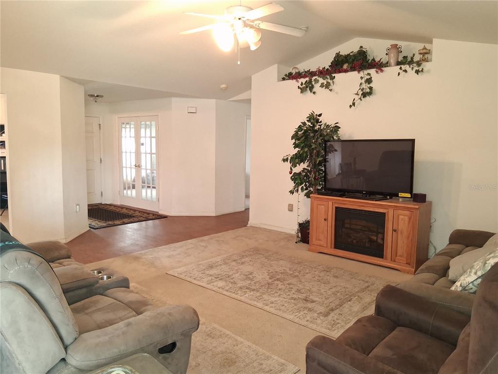 A living room features a television on a wooden stand, carpeted floors, and a ceiling fan — 6759 ASHBURY DRIVE, LAKELAND, FL