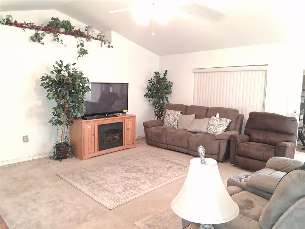 A living room features a fireplace console, brown sofa and recliner, and vaulted ceilings — 6759 ASHBURY DRIVE, LAKELAND, FL