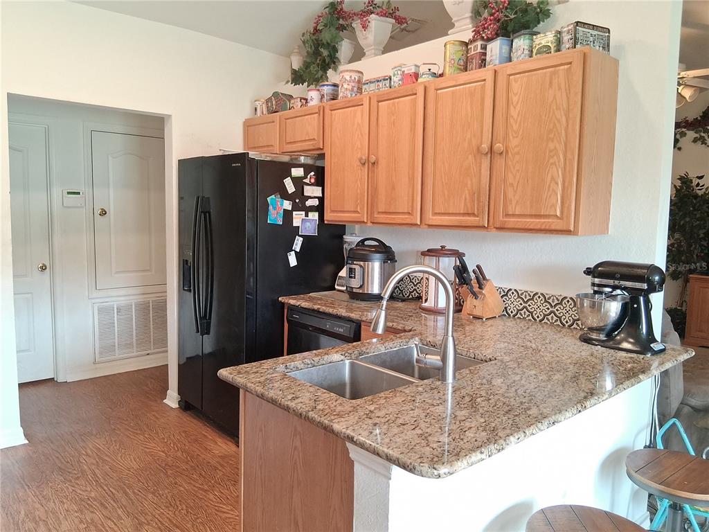 A kitchen features light wood cabinets, granite countertops, a black refrigerator, and a double sink — 6759 ASHBURY DRIVE, LAKELAND, FL