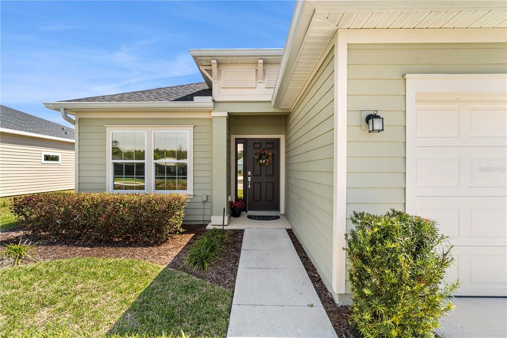 A light green house exterior features a front door, a walkway, and a garage door — 7381 SW 78TH TERRACE, OCALA, FL
