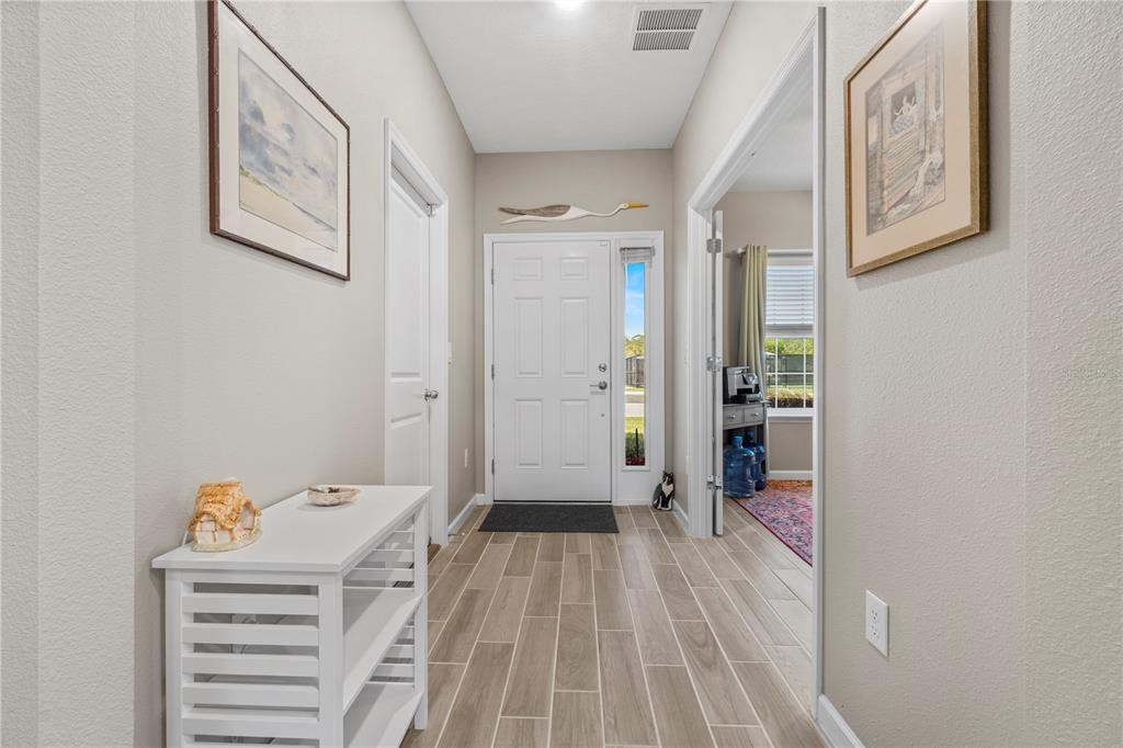 A bright entryway features light wood-look tile flooring, a white front door, and neutral walls — 7381 SW 78TH TERRACE, OCALA, FL