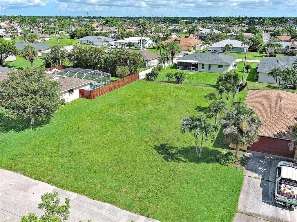 An aerial view shows a vacant, grassy residential lot situated between two houses — 225 SW 46TH TERRACE, CAPE CORAL, FL