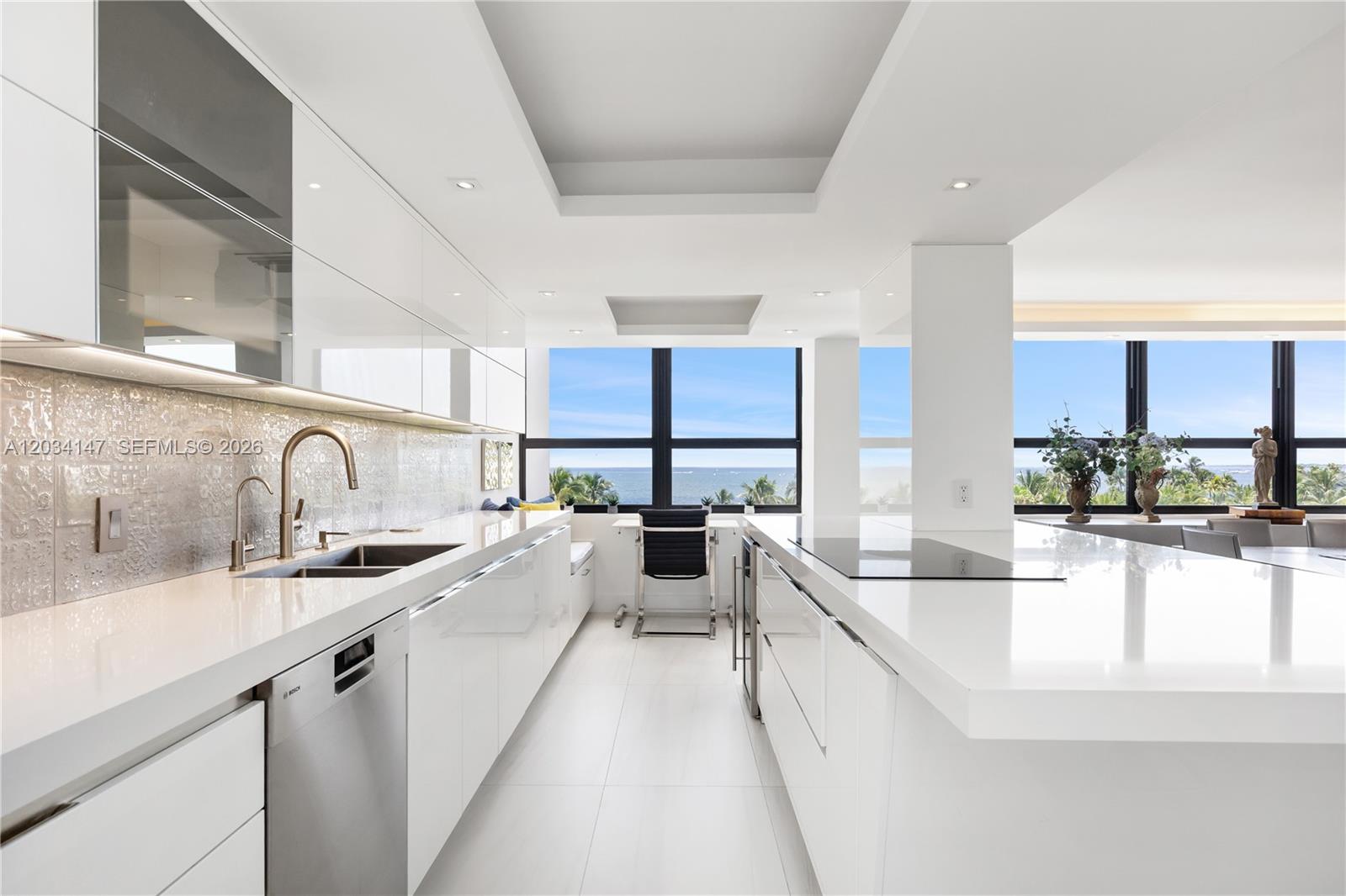A modern white kitchen features a large island, sleek cabinetry, and floor-to-ceiling ocean views — 3 Grove Isle Dr # C502, Miami FL 33133, MIAMI, FL
