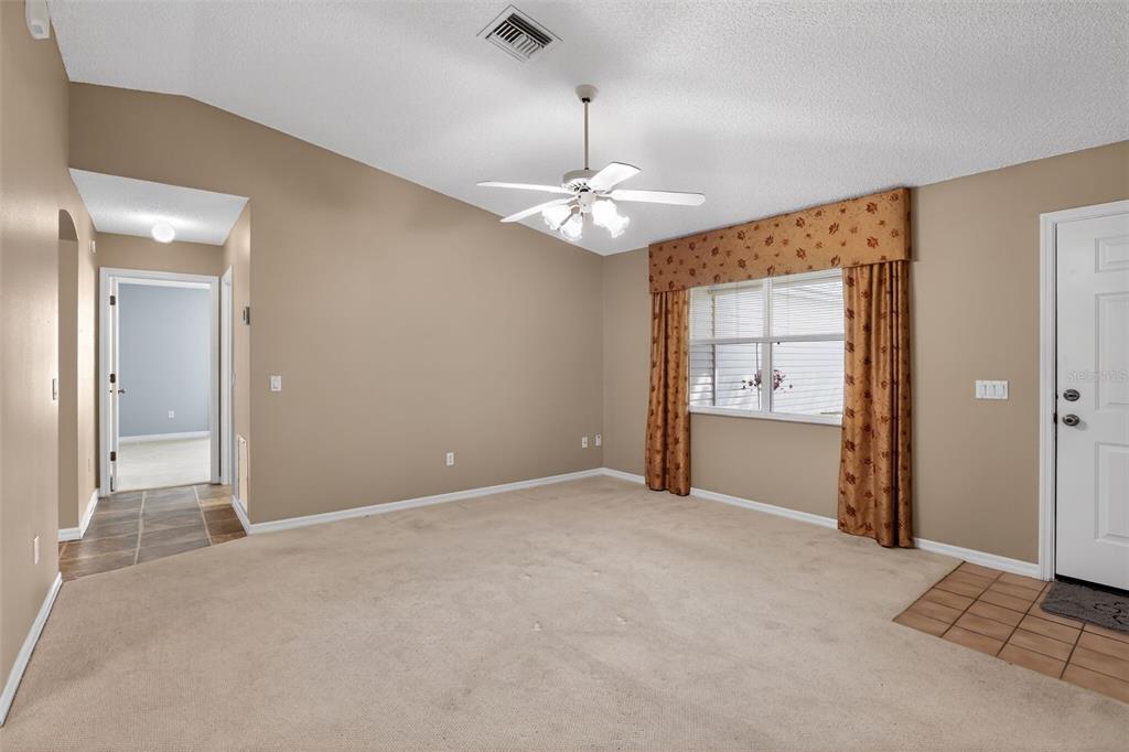 A carpeted living room features a vaulted ceiling, a ceiling fan, and a window with curtains — 728 RIVERA ROAD, THE VILLAGES, FL