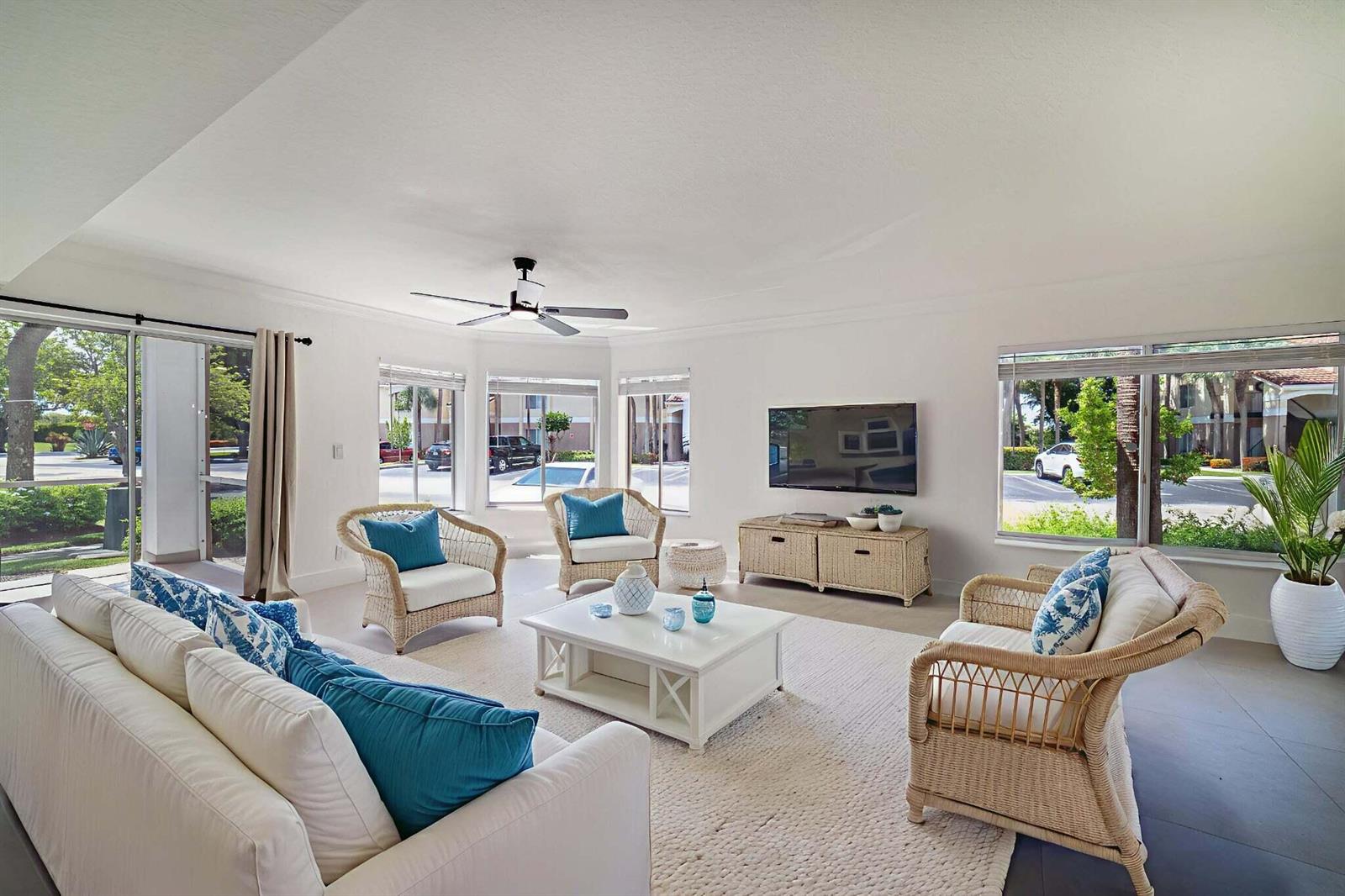 A bright living room features white furniture, wicker accent chairs, and large windows with outdoor views — 815 W Boynton Beach Boulevard # 106, Boynton Beach FL 33426, BOYNTON BEACH, FL