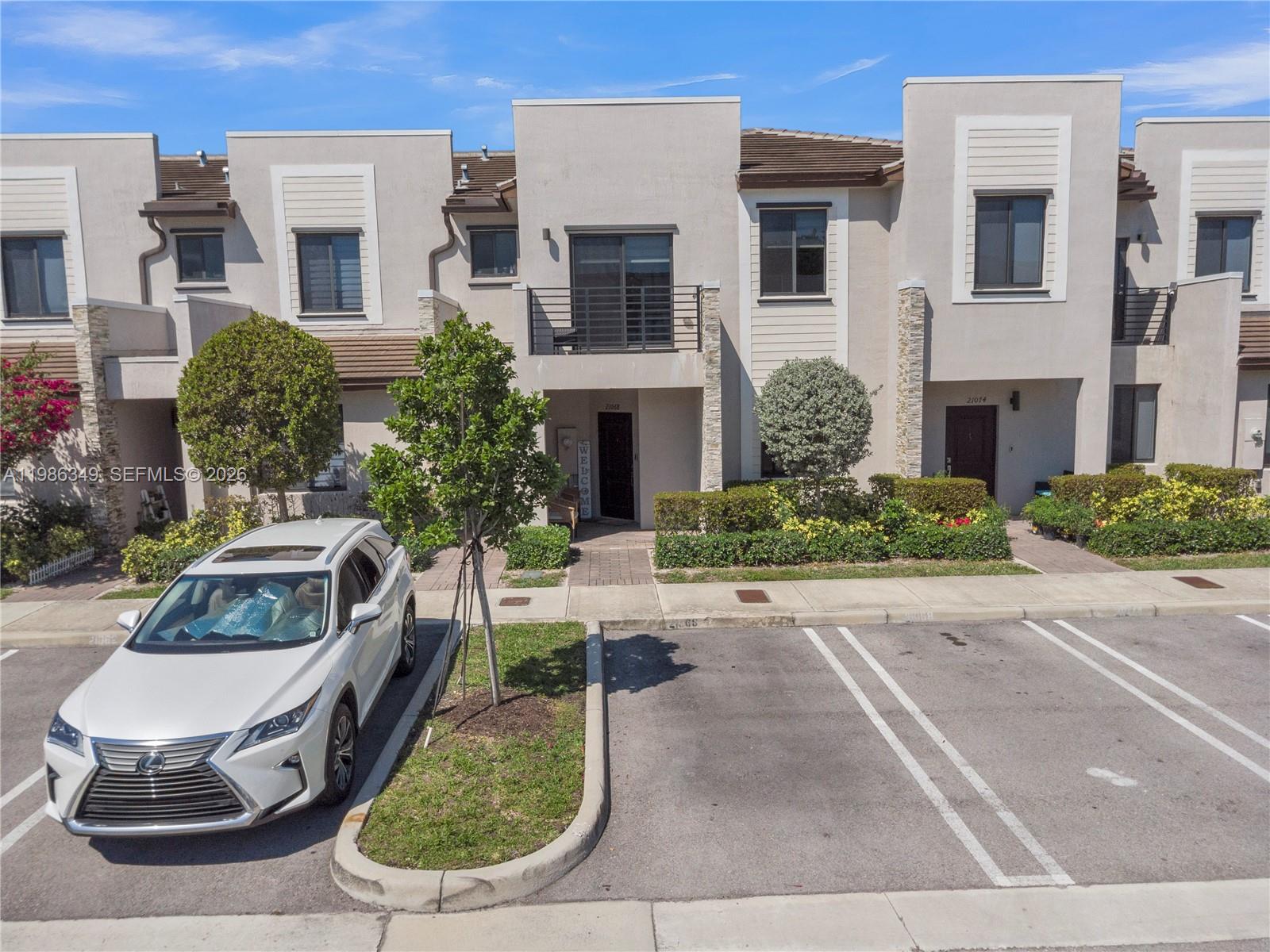 A white car is parked in front of a multi-story townhouse with a balcony — 21068 NE 8th Ave, Miami FL 33179, MIAMI, FL