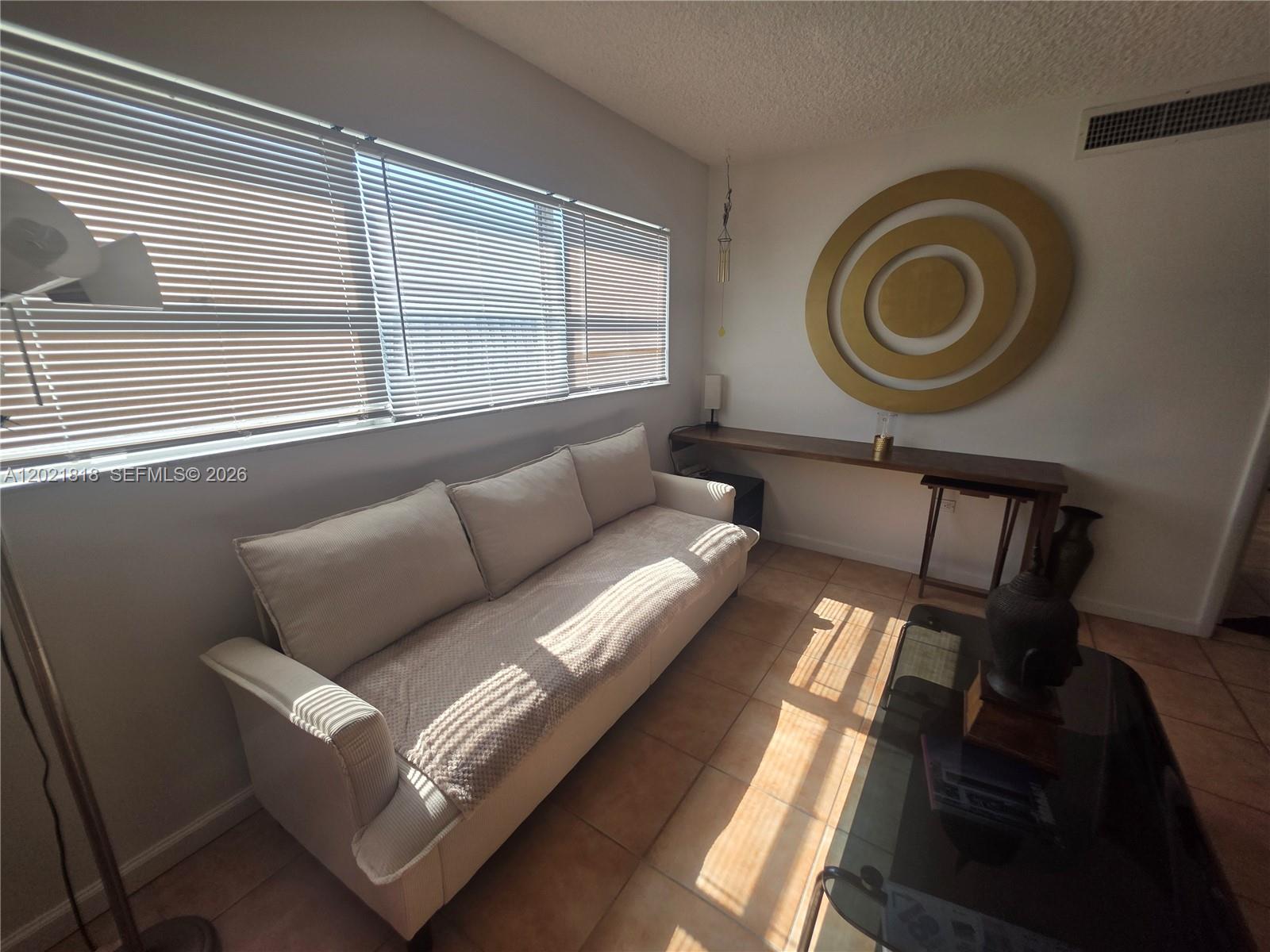 A living room features a beige sofa, a long wooden console table, and tiled floors — 1881 Washington Ave # 6H, Miami Beach FL 33139, MIAMI BEACH, FL