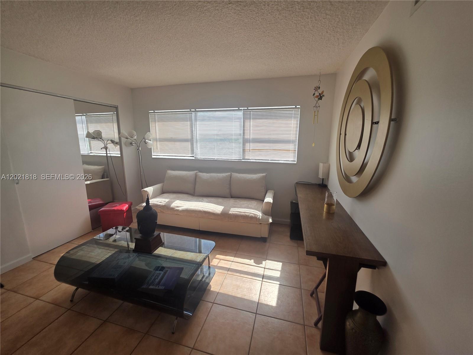 A living room features a beige sofa, a glass coffee table, and a wall-mounted sculpture — 1881 Washington Ave # 6H, Miami Beach FL 33139, MIAMI BEACH, FL