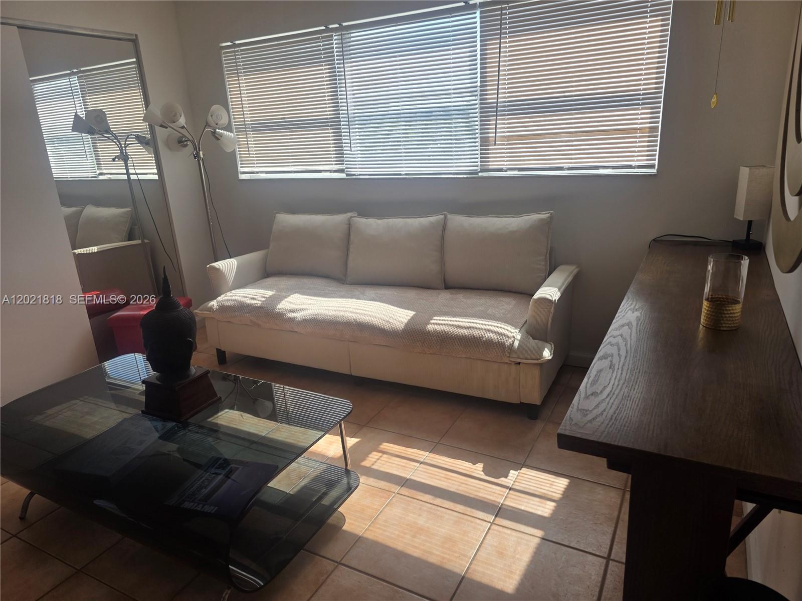 A living room features a beige sofa, a glass coffee table, and a wooden console table — 1881 Washington Ave # 6H, Miami Beach FL 33139, MIAMI BEACH, FL