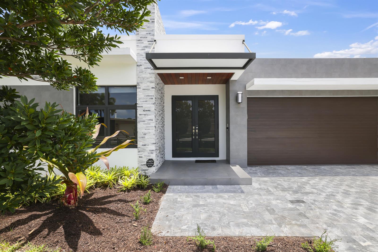 The exterior of a modern house features a stone pillar, double doors, and a garage — 2620 SE 6th Street, Pompano Beach FL 33062, POMPANO BEACH, FL