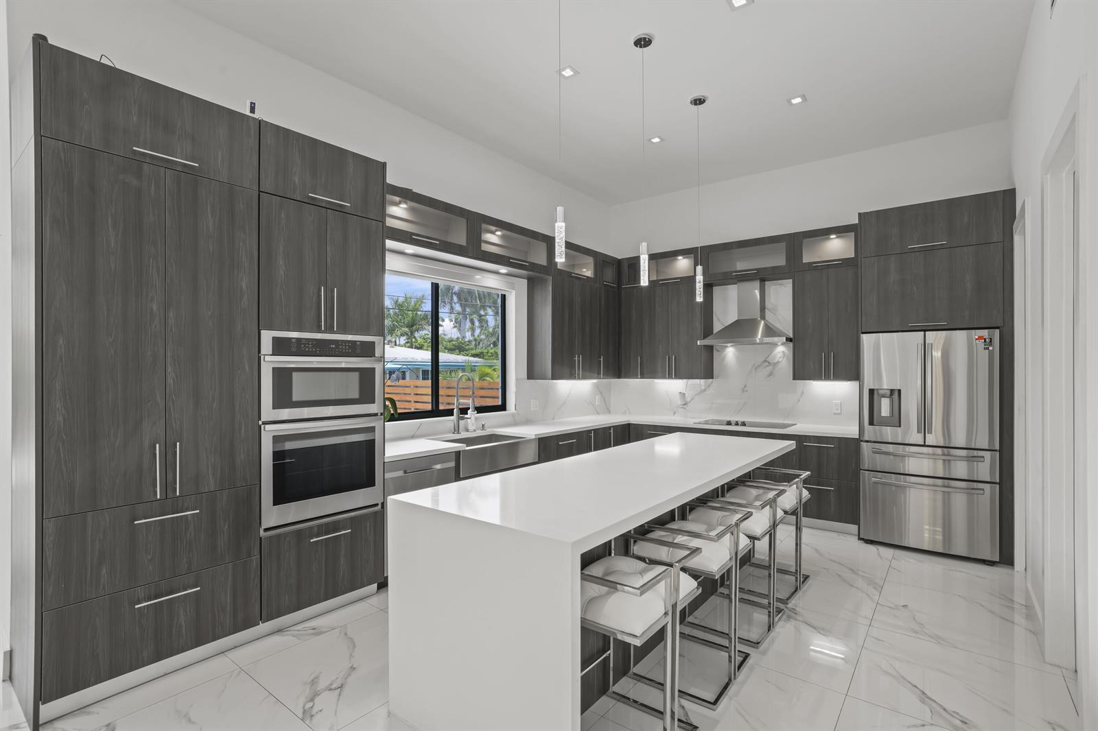 A modern kitchen features dark wood cabinetry, a white waterfall island, and stainless steel appliances — 2620 SE 6th Street, Pompano Beach FL 33062, POMPANO BEACH, FL