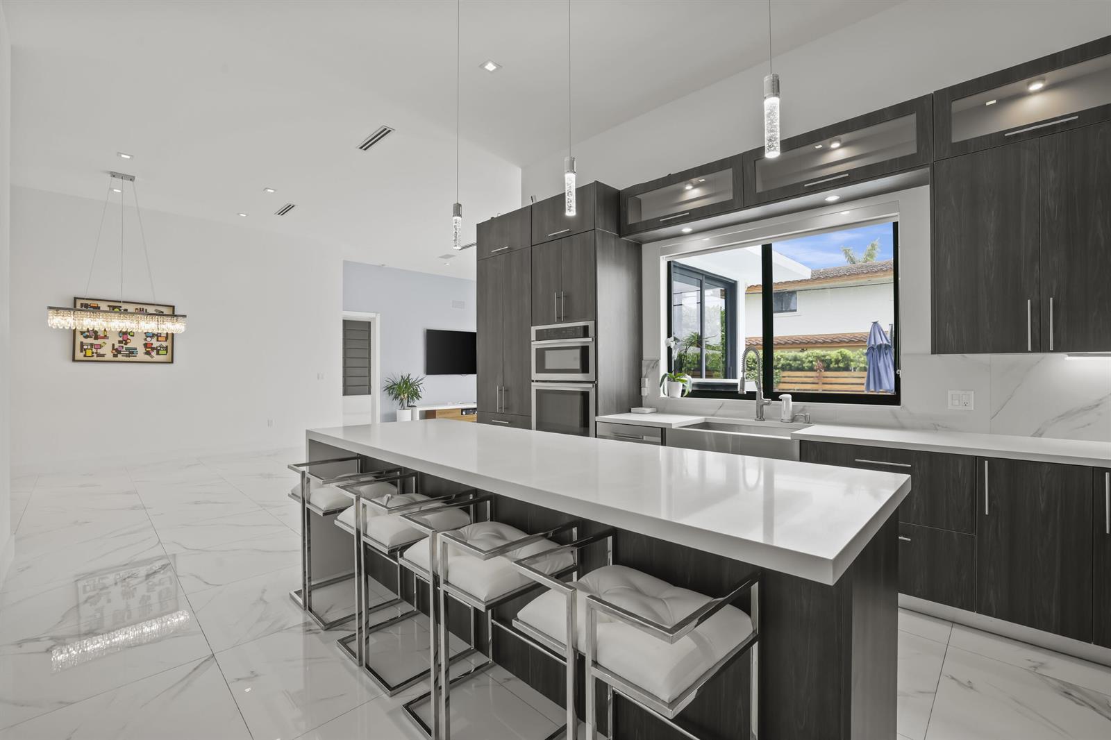 A modern kitchen features dark wood cabinetry, a white quartz island, and white marble flooring — 2620 SE 6th Street, Pompano Beach FL 33062, POMPANO BEACH, FL