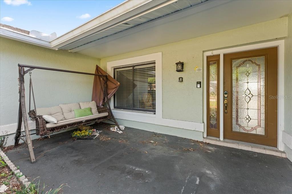 A covered patio features a porch swing, a large window, and a brown front door — 905 STRATFORD MANOR DRIVE, BRANDON, FL