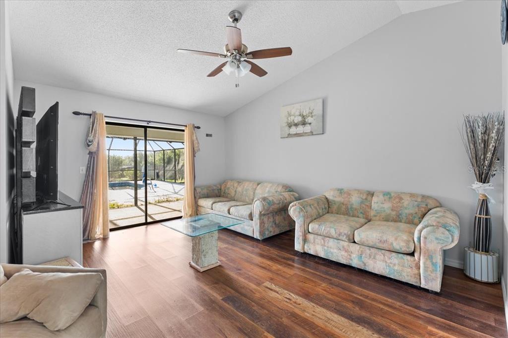A living room features wood-look flooring, two floral sofas, a glass coffee table, and sliding doors — 905 STRATFORD MANOR DRIVE, BRANDON, FL