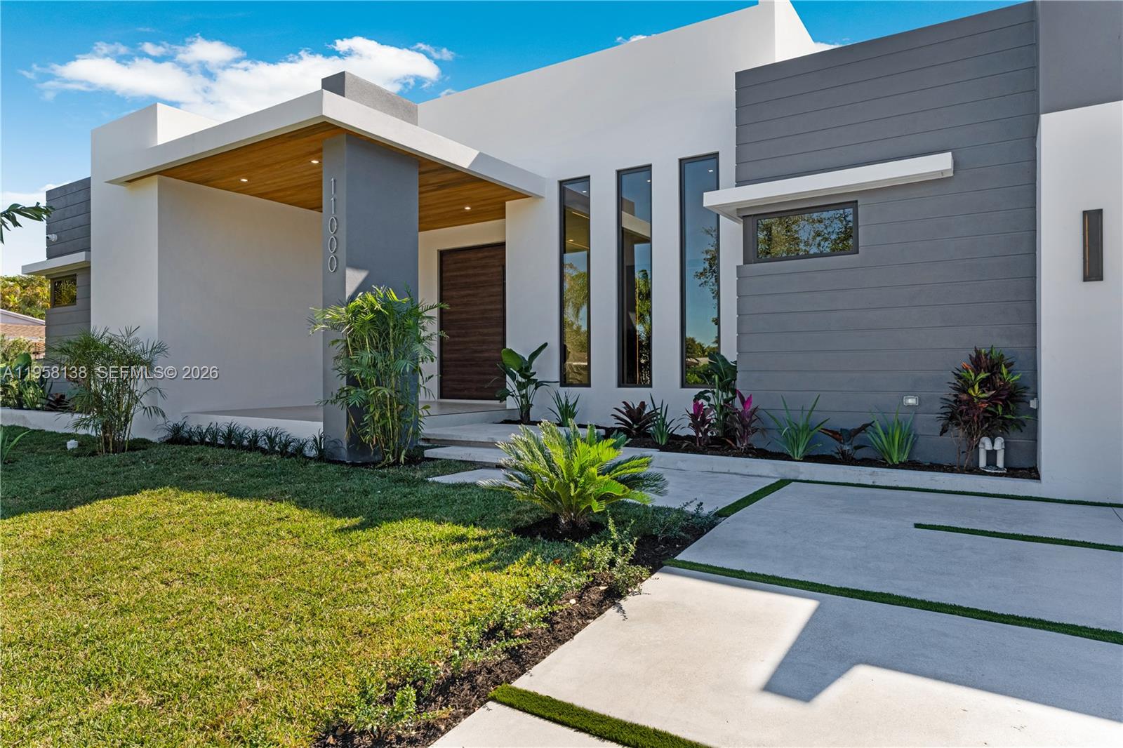 The exterior of a modern home features a covered entryway, gray siding, and vertical windows — 11000 SW 120th St, Miami FL 33176, MIAMI, FL