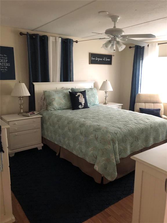 A bedroom features a queen bed with a patterned quilt, dark curtains, and a ceiling fan — 7545 FIRST CIRCLE DRIVE, BROOKSVILLE, FL