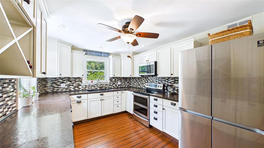 A kitchen features white cabinets, dark countertops, a mosaic tile backsplash, and stainless steel appliances — 5005 24TH AVENUE S, GULFPORT, FL