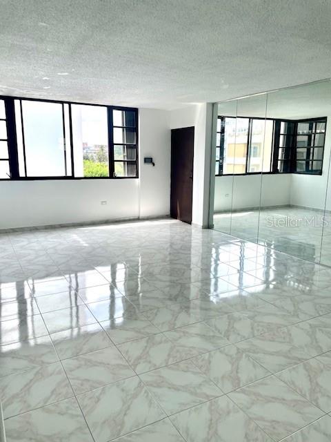 An empty room features white tiled floors, large windows, and a mirrored wall — 18 MARSEILLES UNIT 4B, SAN JUAN, PR