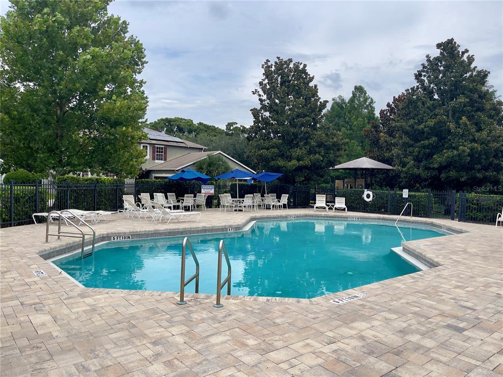 A swimming pool with a paved deck, lounge chairs, and umbrellas in a residential area — 834 SENECA MEADOWS ROAD, WINTER SPRINGS, FL