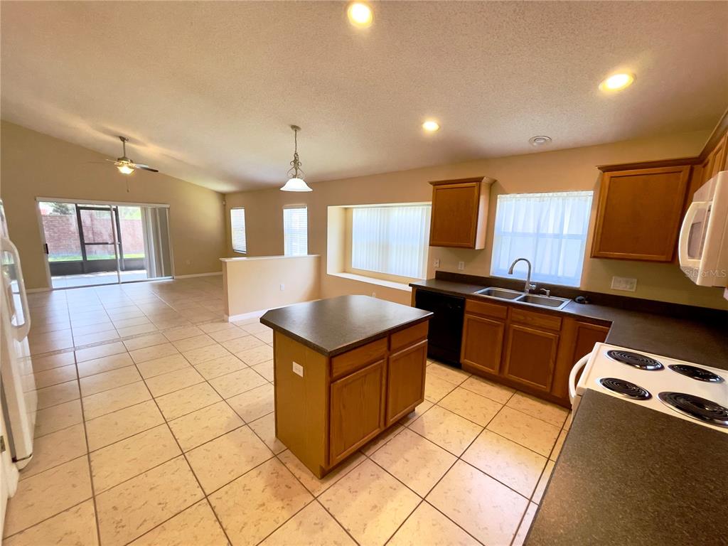 A kitchen with wood cabinets and a center island opens to a tiled living area — 834 SENECA MEADOWS ROAD, WINTER SPRINGS, FL