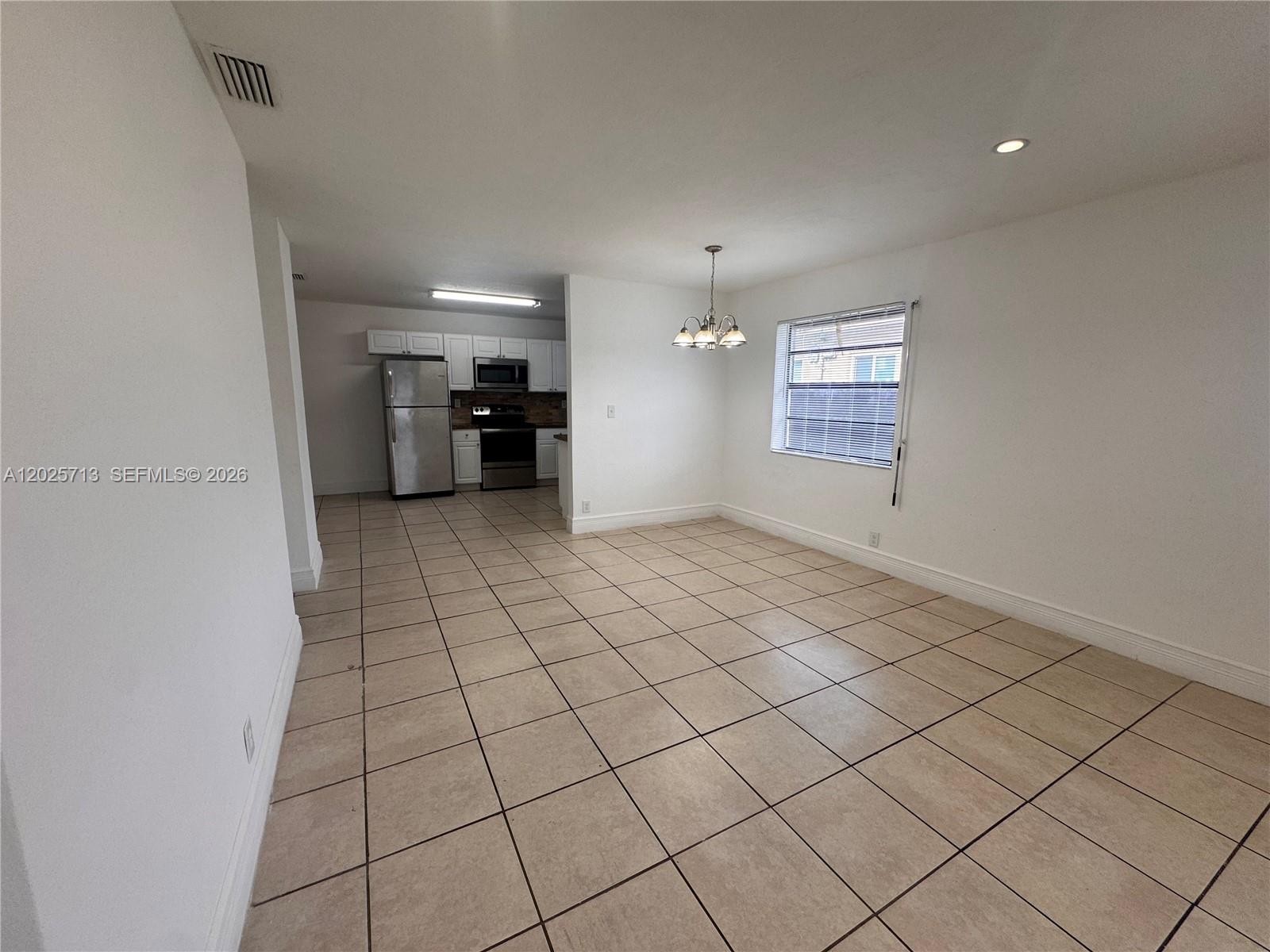 An open-concept dining area with tile flooring leads into a kitchen with white cabinets — 407 NW 7th Ct, Hallandale Beach FL 33009, HALLANDALE BEACH, FL