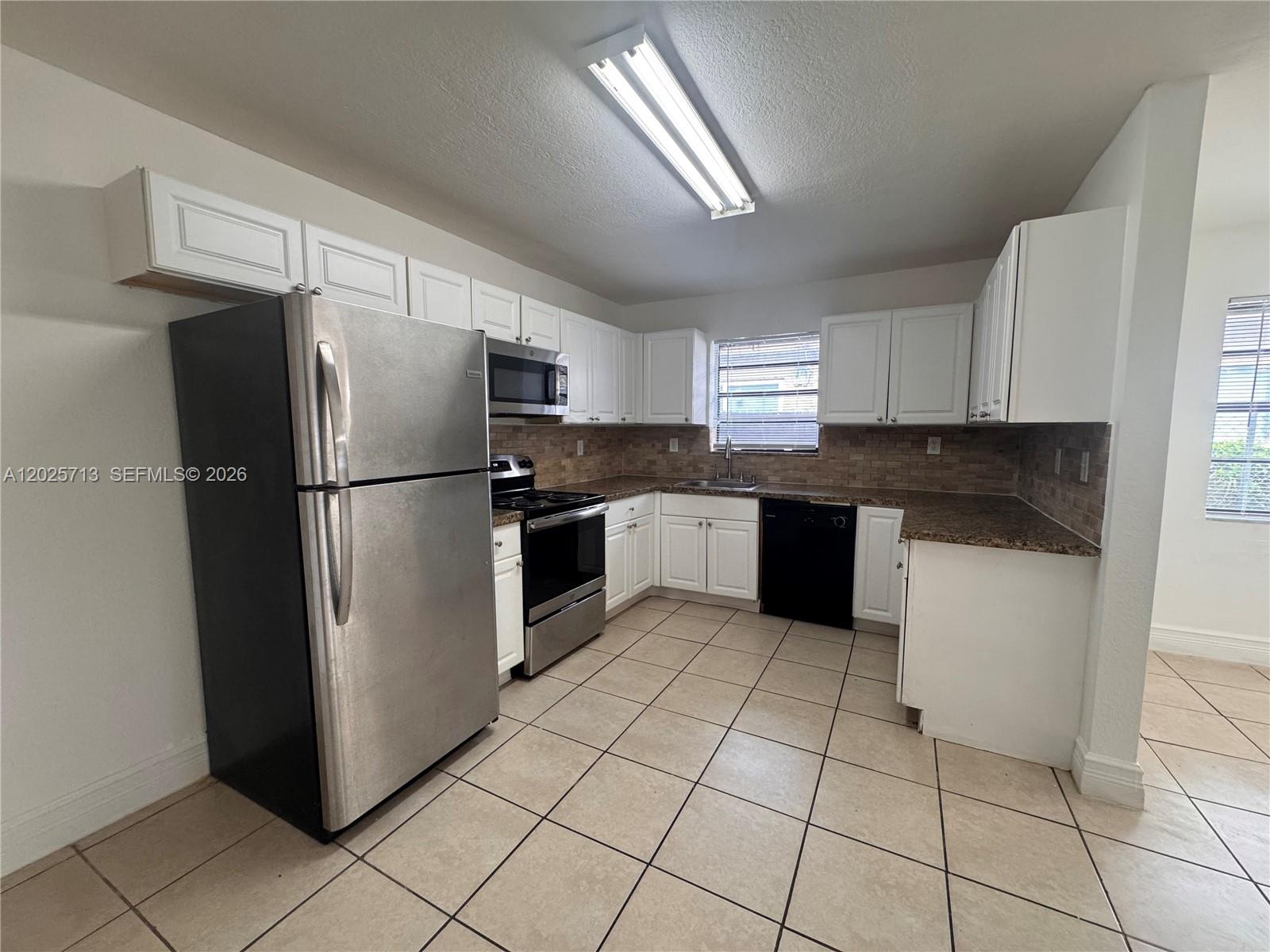 A kitchen features white cabinets, stainless steel appliances, a black dishwasher, and tiled flooring — 407 NW 7th Ct, Hallandale Beach FL 33009, HALLANDALE BEACH, FL